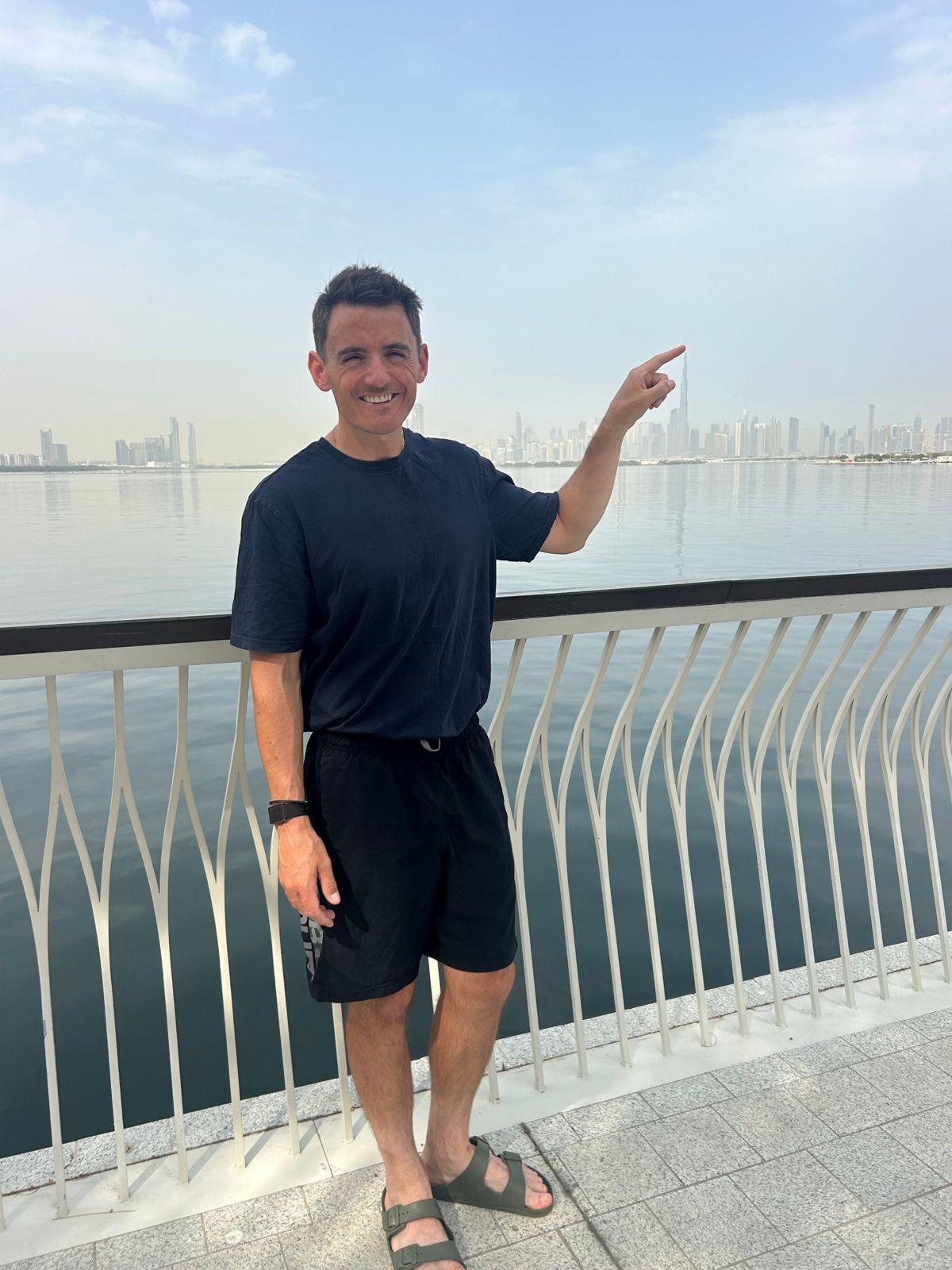 Kevin Walsh on the Dubai Creek waterfront, pointing at the Burj Khalifa